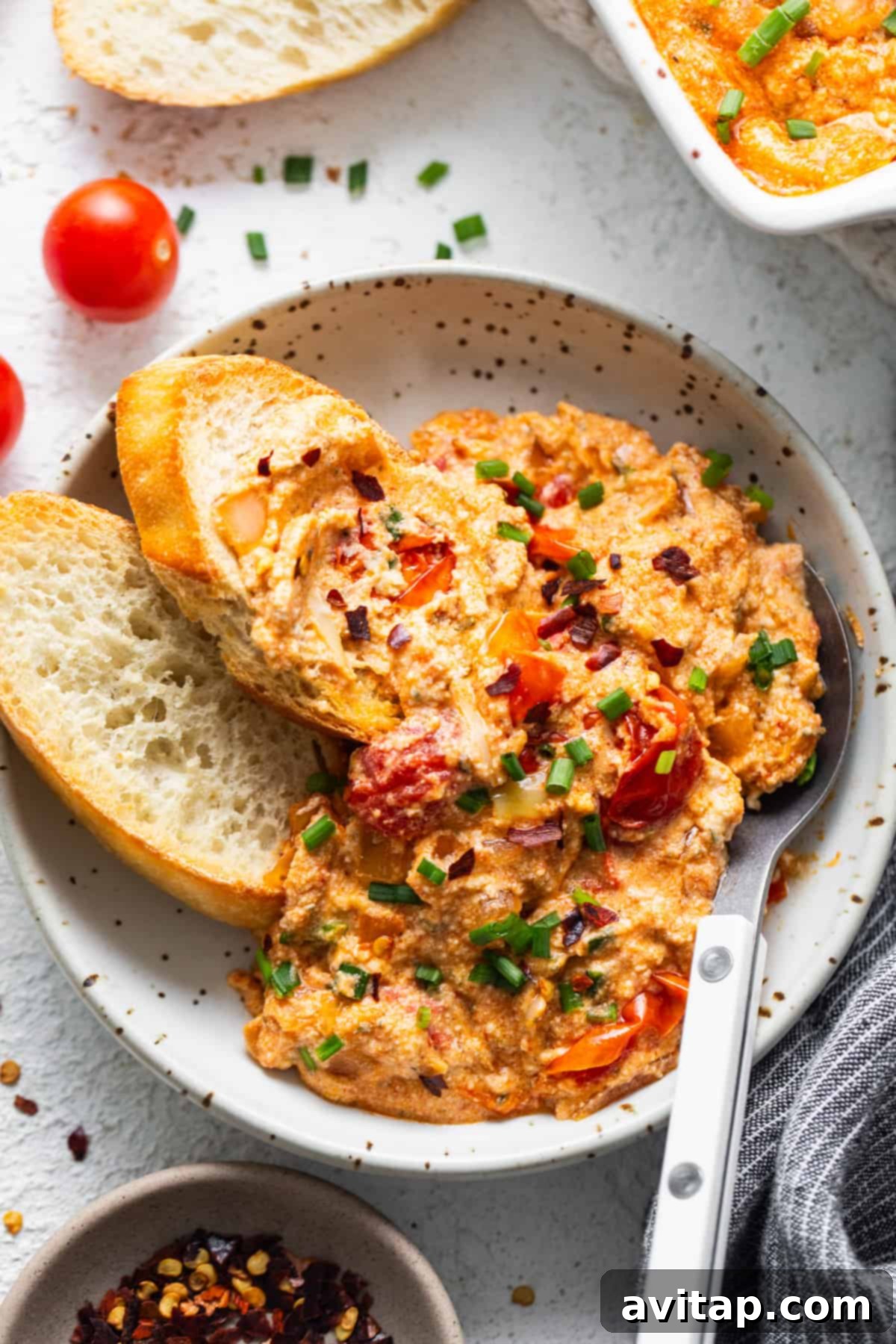 Creamy Roasted Garlic Boursin Bake 8 A beautifully plated serving of Baked Boursin Dip, garnished with fresh chives and red pepper flakes, accompanied by artisan bread slices and vibrant cherry tomatoes.