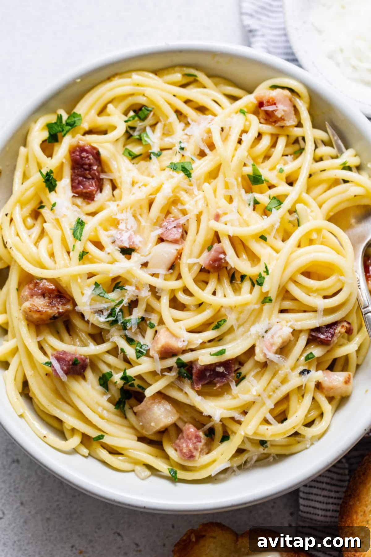 Easy Weeknight Carbonara 5 A close-up of creamy pasta carbonara with pancetta and cheese in a white bowl, garnished with black pepper.