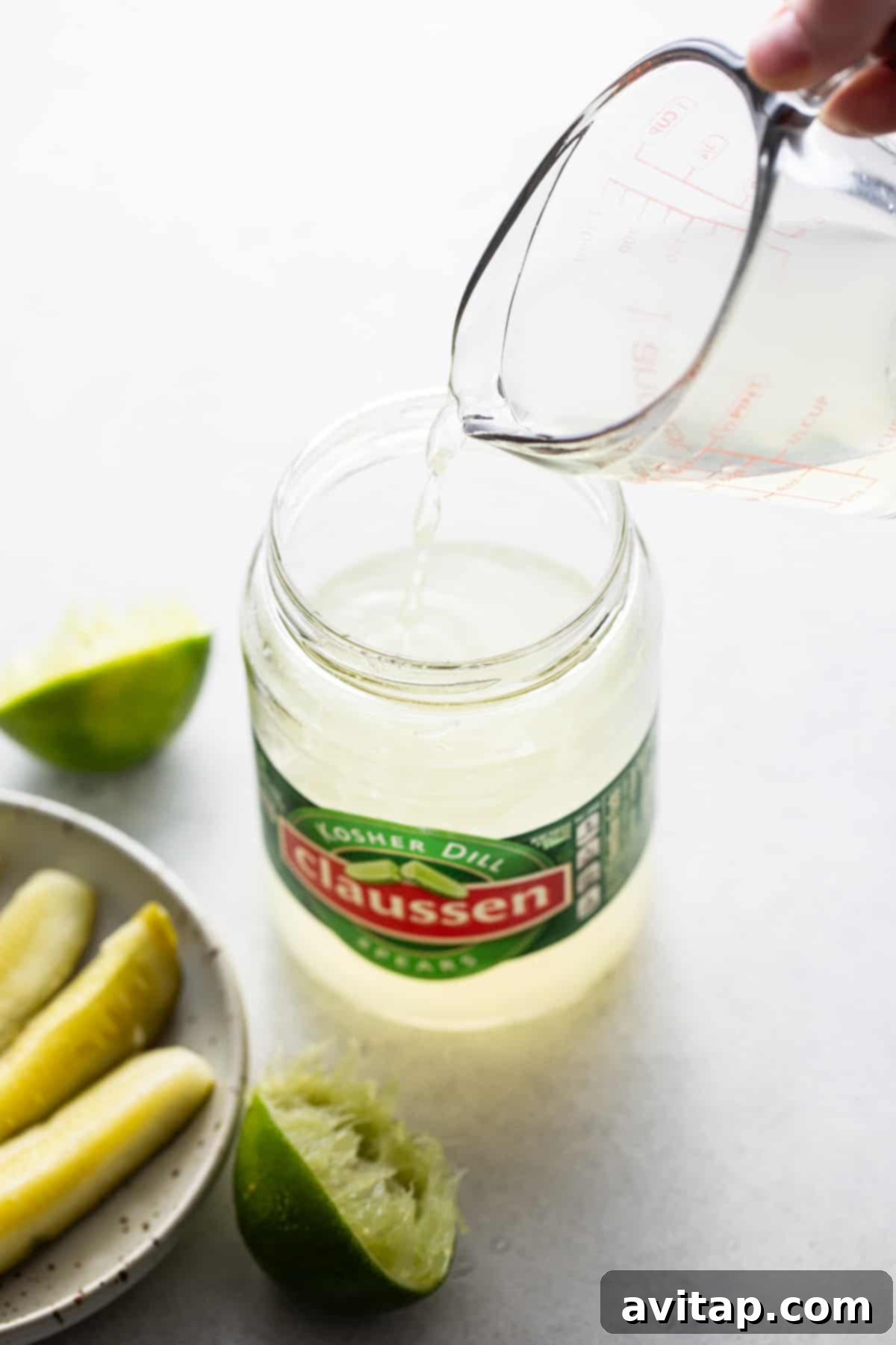 A person pouring a liquid into a jar of pickles.