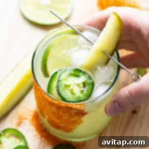 A hand holding a glass of drink with a pickle and lime.