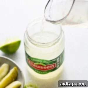 A person pouring a liquid into a jar of pickles.