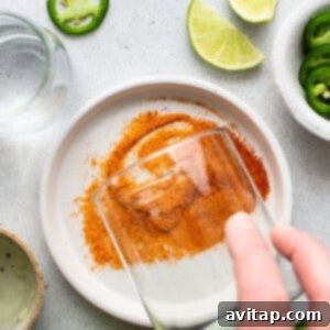 A person sprinkling salt on a glass with limes and jalapenos.