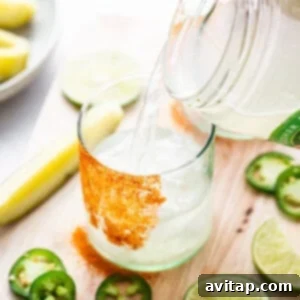 A person pouring a drink into a glass with limes and jalapenos.