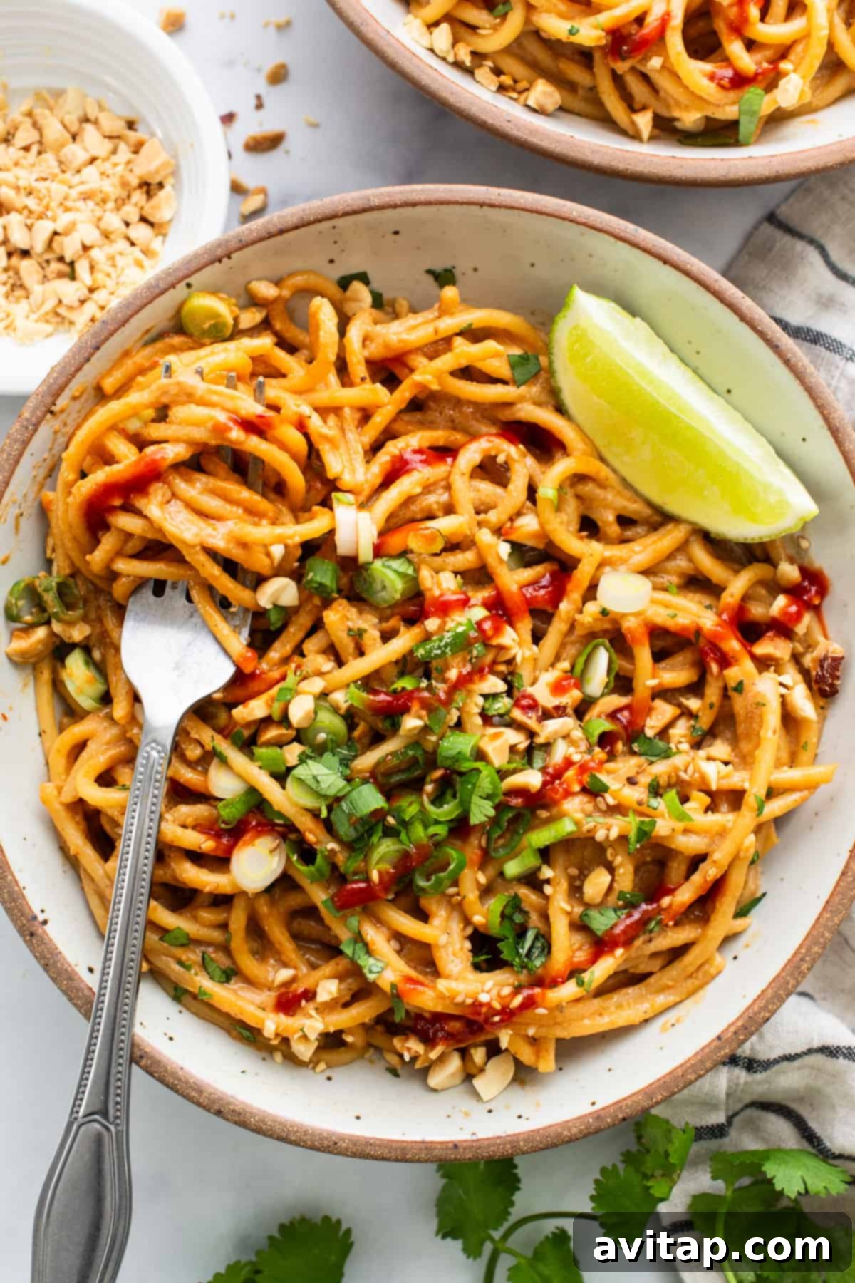 A close-up shot of Thai peanut noodles in a bowl with a fork, ready to be eaten.
