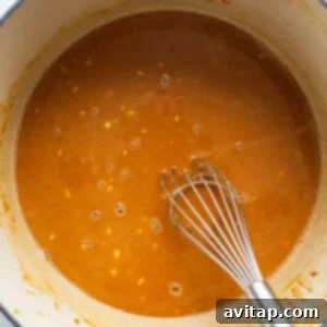 A pot containing the creamy peanut sauce with a whisk, ready for noodles.