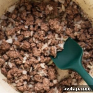 Ground beef and diced onions cooking in a large pot, beginning to brown and release their aromas, forming the base of the ramen dish.