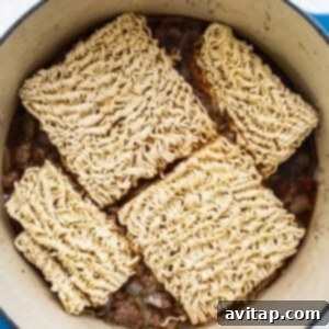 Ramen noodles being submerged into a simmering pot of beef broth and aromatic sauce, ready to cook and absorb the rich flavors.