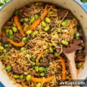 A mix of cooked ramen noodles, ground beef, bell peppers, and edamame simmering together in a pot, demonstrating the one-pot cooking process.