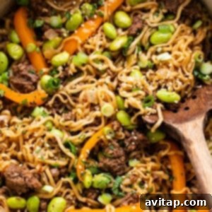 A large pan filled with the completed one-pot ground beef ramen noodles, glistening with sauce and ready to be scooped, alongside a wooden spoon.