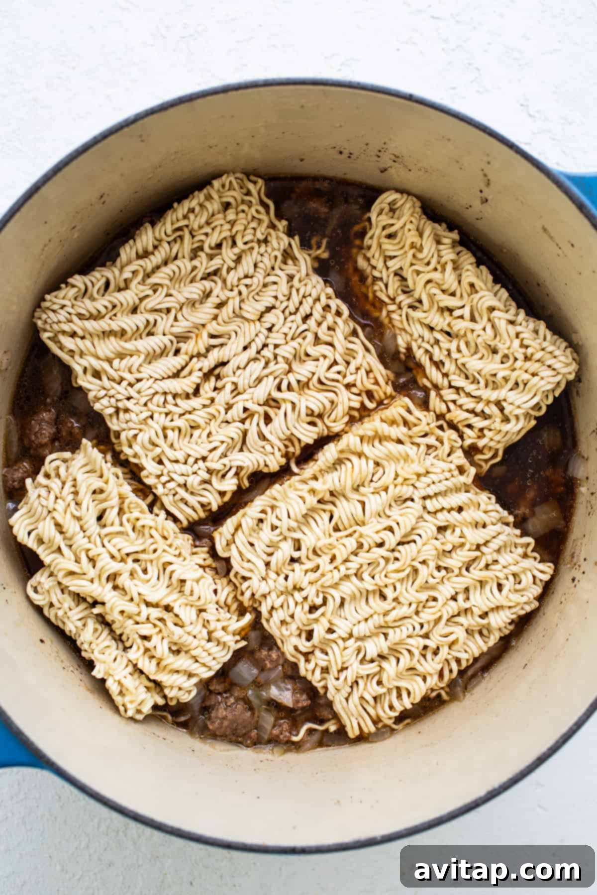 Uncooked ramen noodles resting in a large cooking pot, ready to absorb the flavorful broth and beef, highlighting the simplicity of this one-pot preparation.
