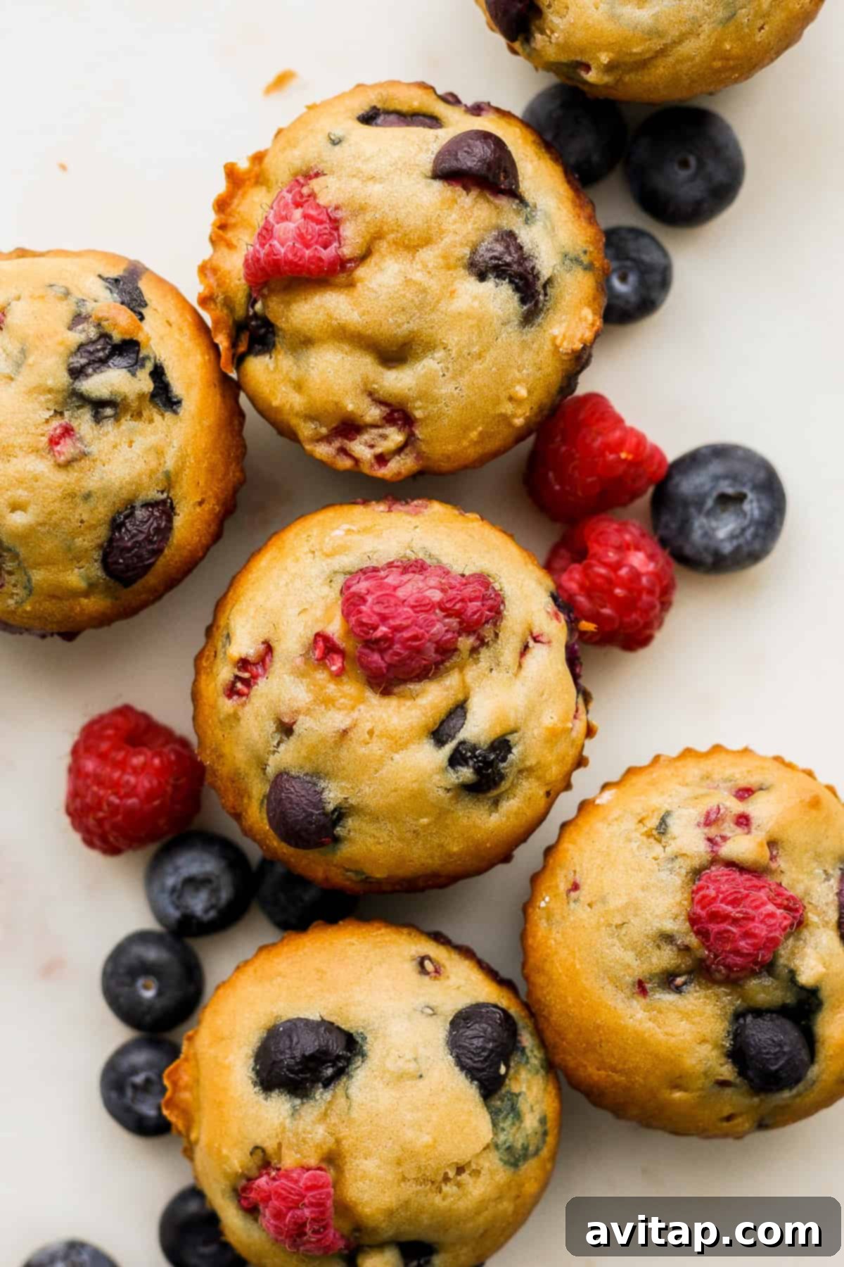 A group of fluffy Greek Yogurt Berry Muffins with raspberries and blueberries on top, ready to be enjoyed.