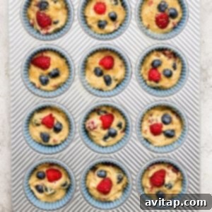 A muffin tin filled with unbaked muffin batter, topped with fresh berries, poised for baking.