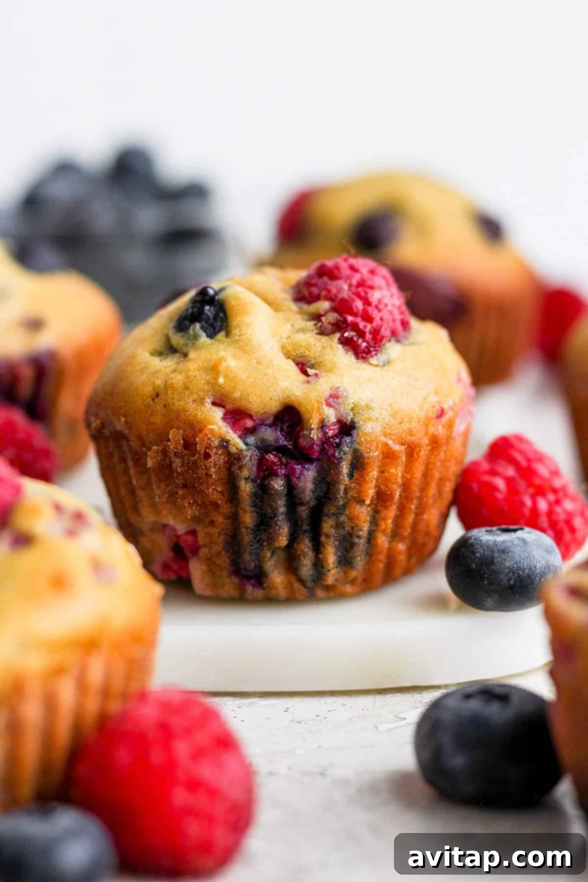 Delicious Greek Yogurt Berry Muffins with blueberries and raspberries, arranged on a rustic wooden cutting board.