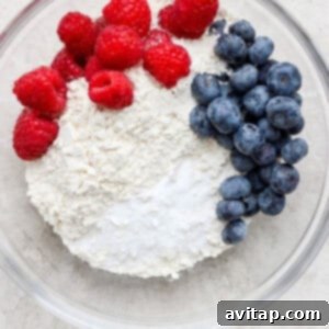 A bowl containing dry ingredients: flour, baking soda, salt, and colorful fresh blueberries and raspberries.