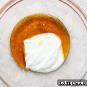 A glass bowl with a creamy mixture, likely honey and Greek yogurt, being whisked until smooth.