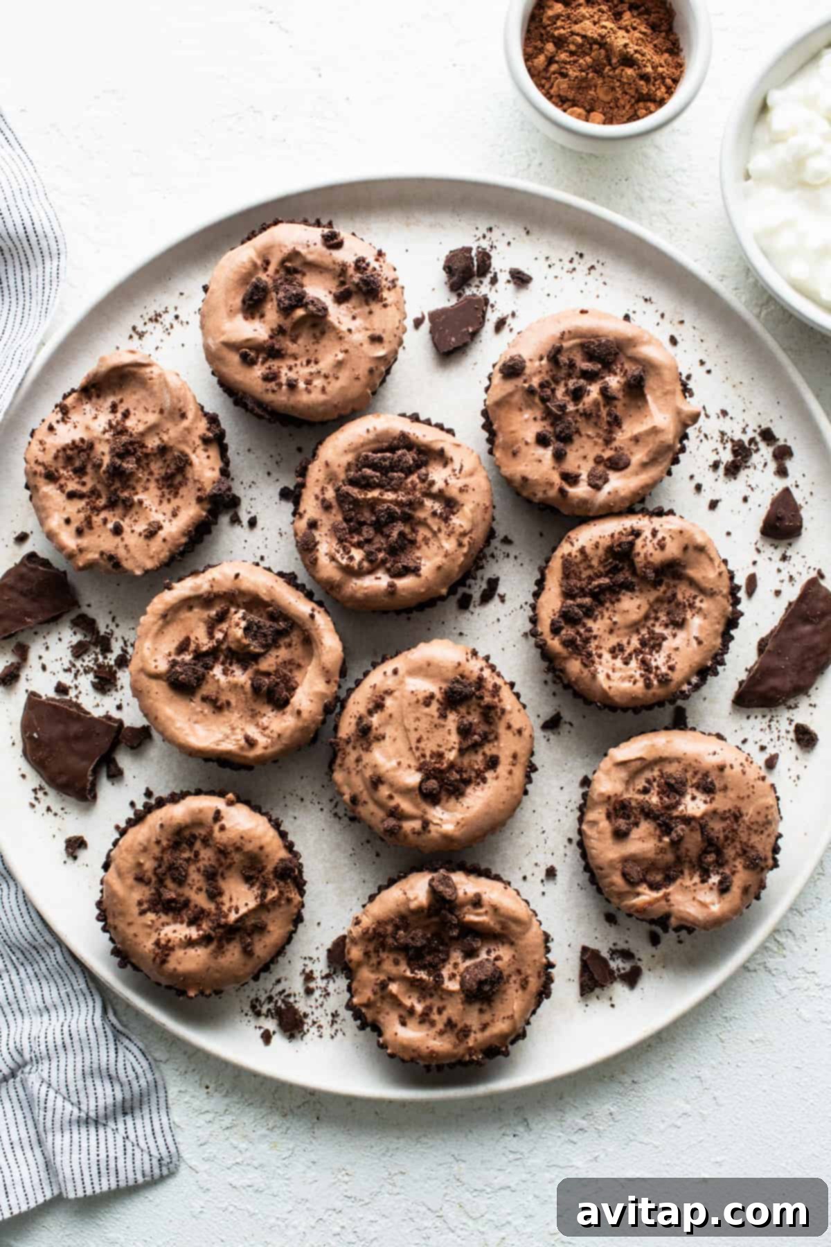 Exquisitely arranged chocolate mousse cups with chocolate frosting and a dusting of cocoa, presented on a pristine white plate, inviting indulgence.