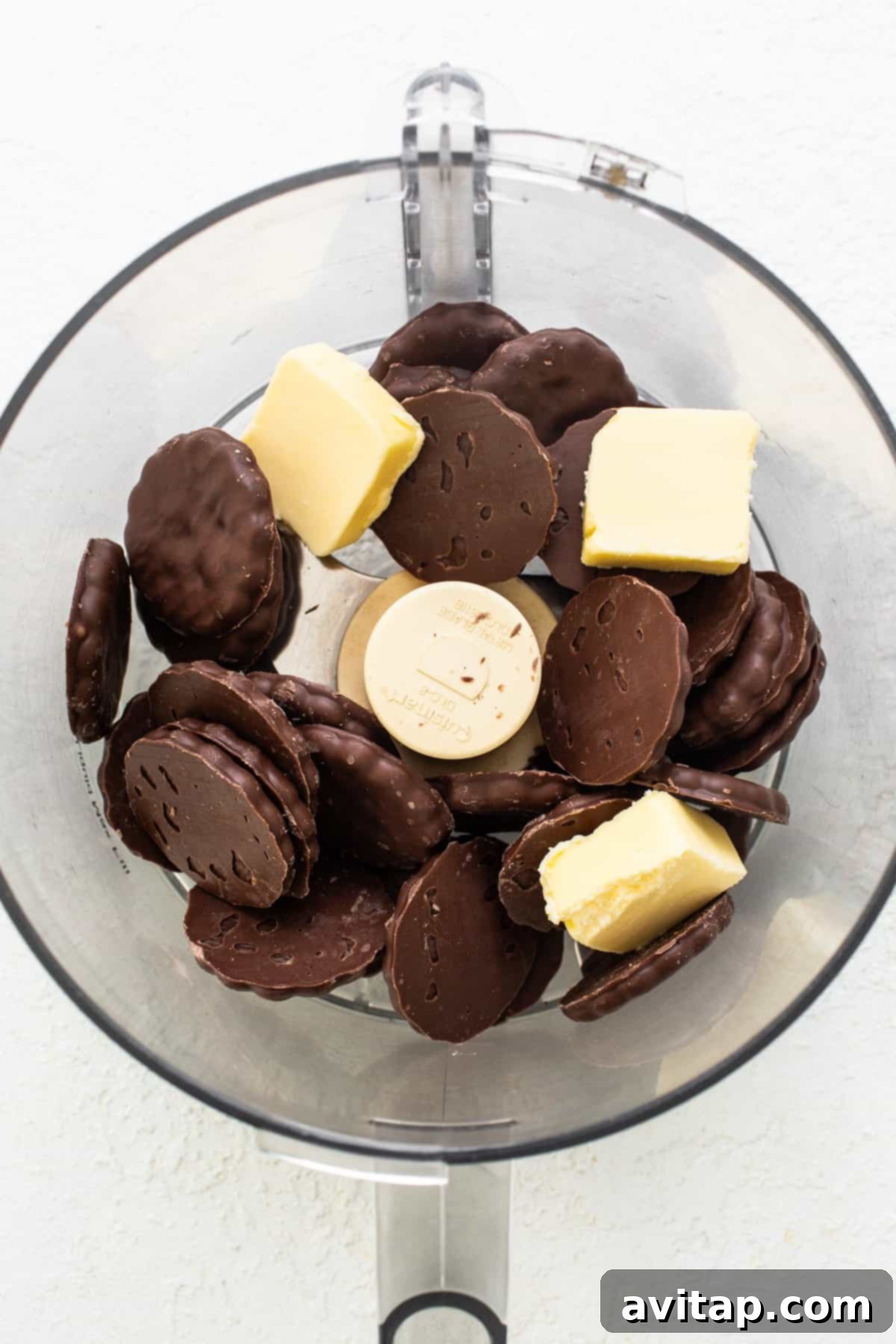 A glass bowl showcasing chunks of dark chocolate and pats of butter, indicating the start of the chocolate melting process for a rich dessert.