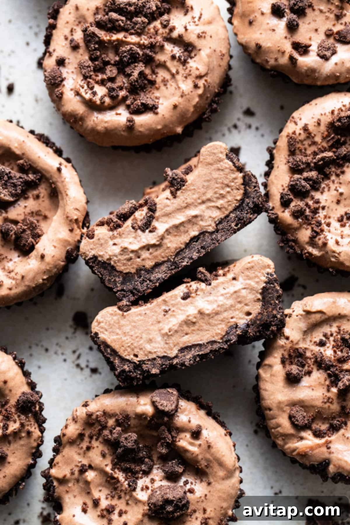 A selection of chocolate mousse cups, with one having a spoonful taken out, revealing the creamy interior and the crisp cookie crust.