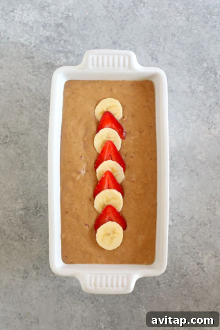 Effortless Strawberry Banana Bread 4 Strawberry banana bread batter in a loaf pan, ready for baking, with fruit slices on top.