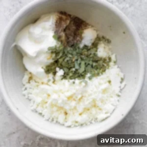 A bowl of crumbled feta cheese mixed with seasonings and yogurt on a textured surface.