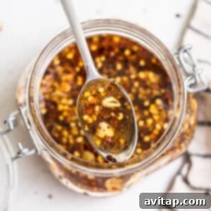 A spoonful of chile-infused honey being held over a glass jar.