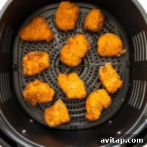 Crispy chicken pieces cooking in an air fryer basket.