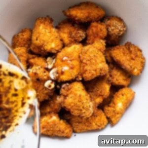 A hand drizzling hot honey sauce over crispy chicken pieces in a mixing bowl.