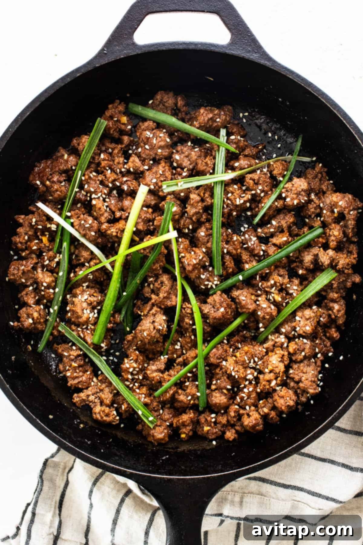 Korean Beef Bowls 3 Perfectly cooked Korean ground beef, garnished generously with vibrant green onions and toasted sesame seeds, served in a rustic cast iron skillet.