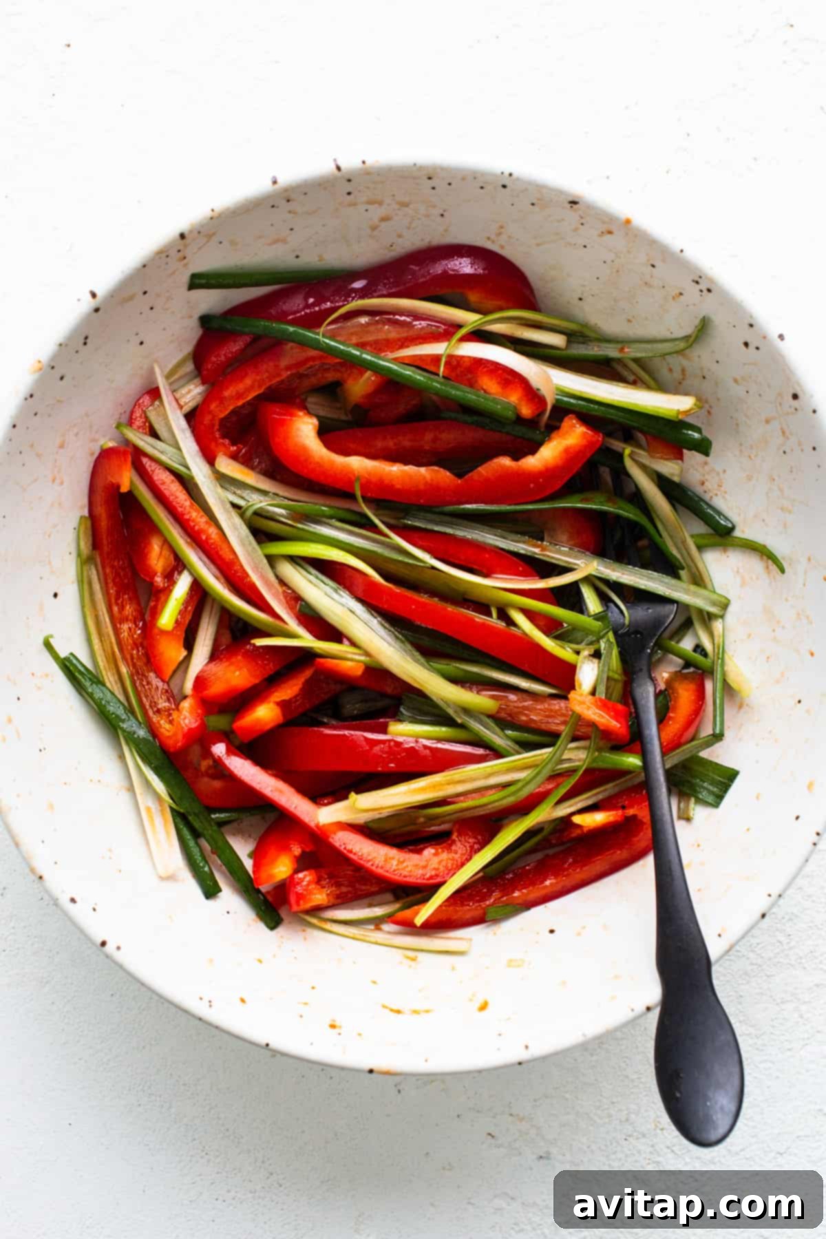 A vibrant bowl filled with freshly sliced red bell peppers and crisp green onions, awaiting its role in the Korean ground beef salad, with a spoon nearby.