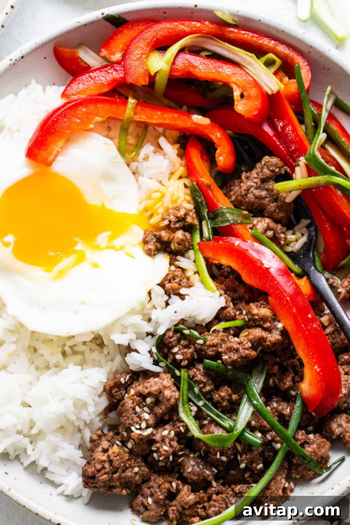 A colorful Bibimbap bowl featuring Korean ground beef, an assortment of fresh vegetables, and a perfectly cooked sunny-side-up egg, inviting diners to mix and enjoy.