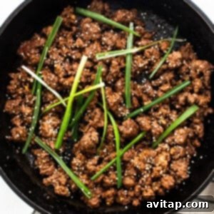 Cooked Korean ground beef garnished with green onions and sesame seeds in a cast iron skillet, ready to be served.