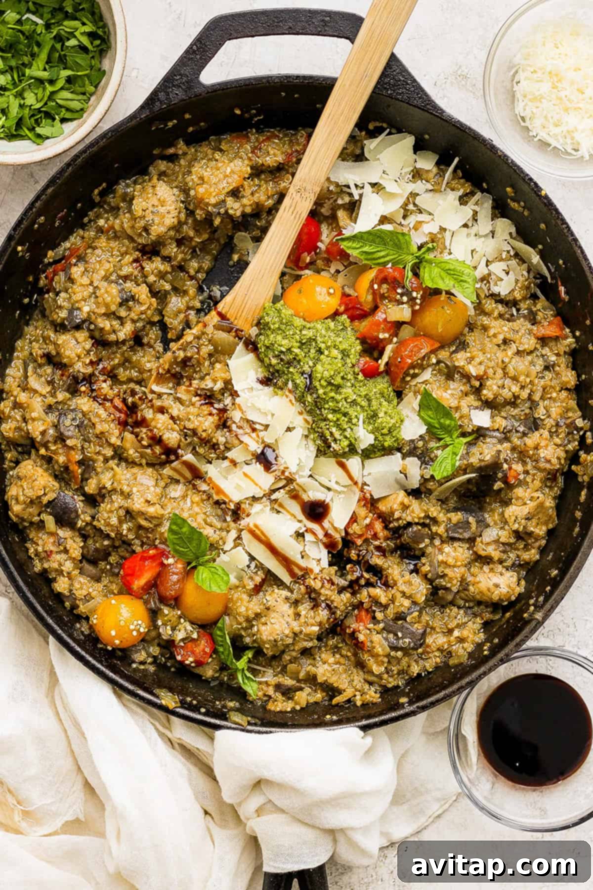 A skillet full of vegetables and herbs with a wooden spoon, showcasing the vibrant colors of the pesto chicken quinoa skillet.