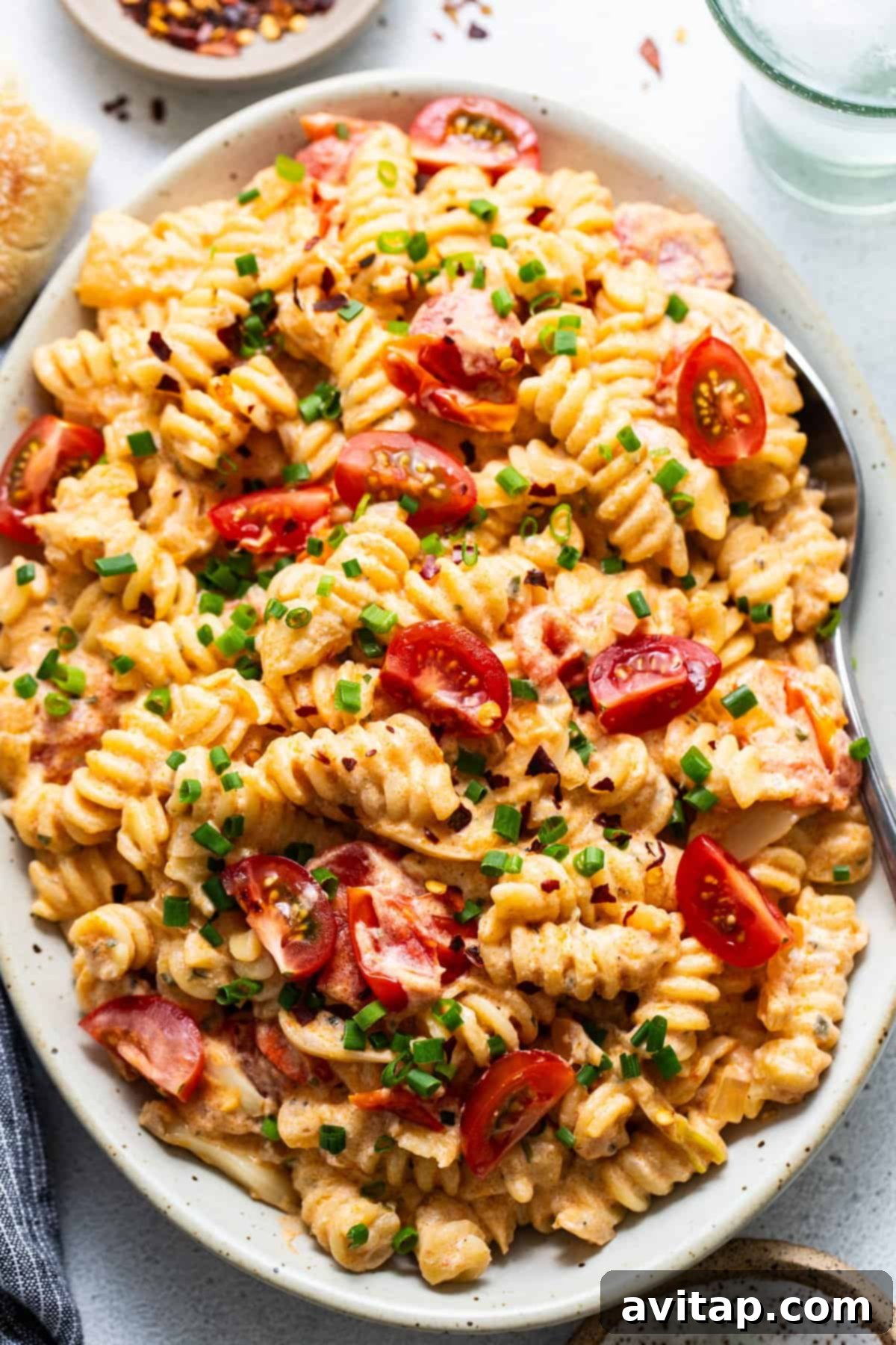 A plate of creamy pasta salad with sliced cherry tomatoes and chopped green onions.