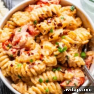 A rustic bowl of creamy baked macaroni and cheese, topped with juicy sliced tomatoes and a sprinkle of fresh chopped green onions.