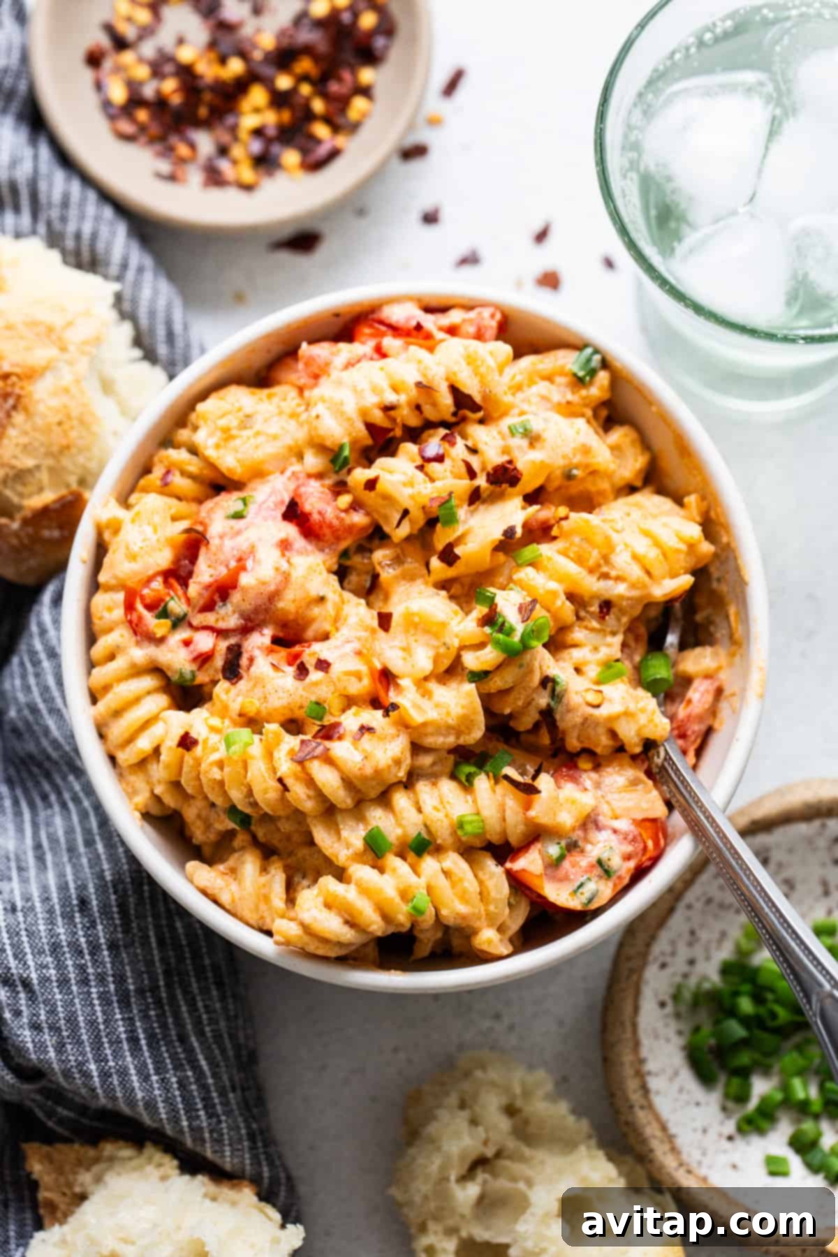 A beautifully presented bowl of creamy tomato pasta, garnished with fresh green onions, accompanied by crusty bread and a refreshing glass of water on a rustic wooden surface.