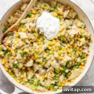 A skillet filled with corn and sour cream, topped with cheese, ready for the broiler.