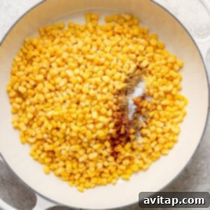 Corn kernels caramelizing in a white pan, seasoned with spices.