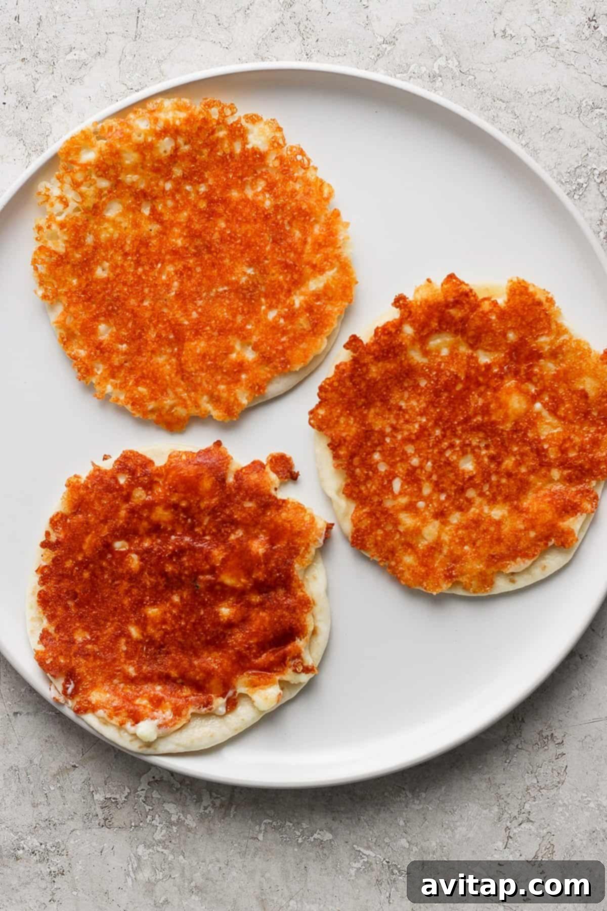 Three golden-brown cheese pancakes on a white plate with a light textured background.
