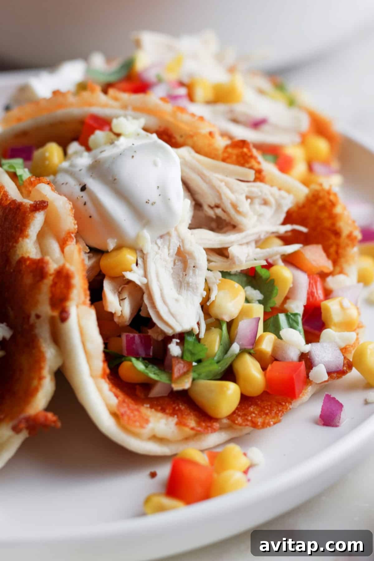 Plate with chicken tacos garnished with corn, diced tomatoes, onions, fresh cilantro, and a dollop of sour cream.