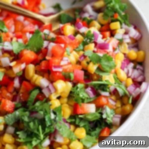 A vibrant bowl of corn salsa with diced red onions, chopped tomatoes, and fresh cilantro.