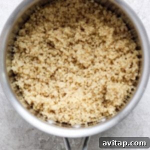 A saucepan filled with fluffy, cooked quinoa, steaming gently as it cools, ready for incorporation into the fresh salad.
