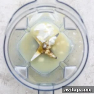 Initial dressing ingredients, including liquids, garlic, and Greek yogurt, being smoothly blended in a blender to create a creamy base.