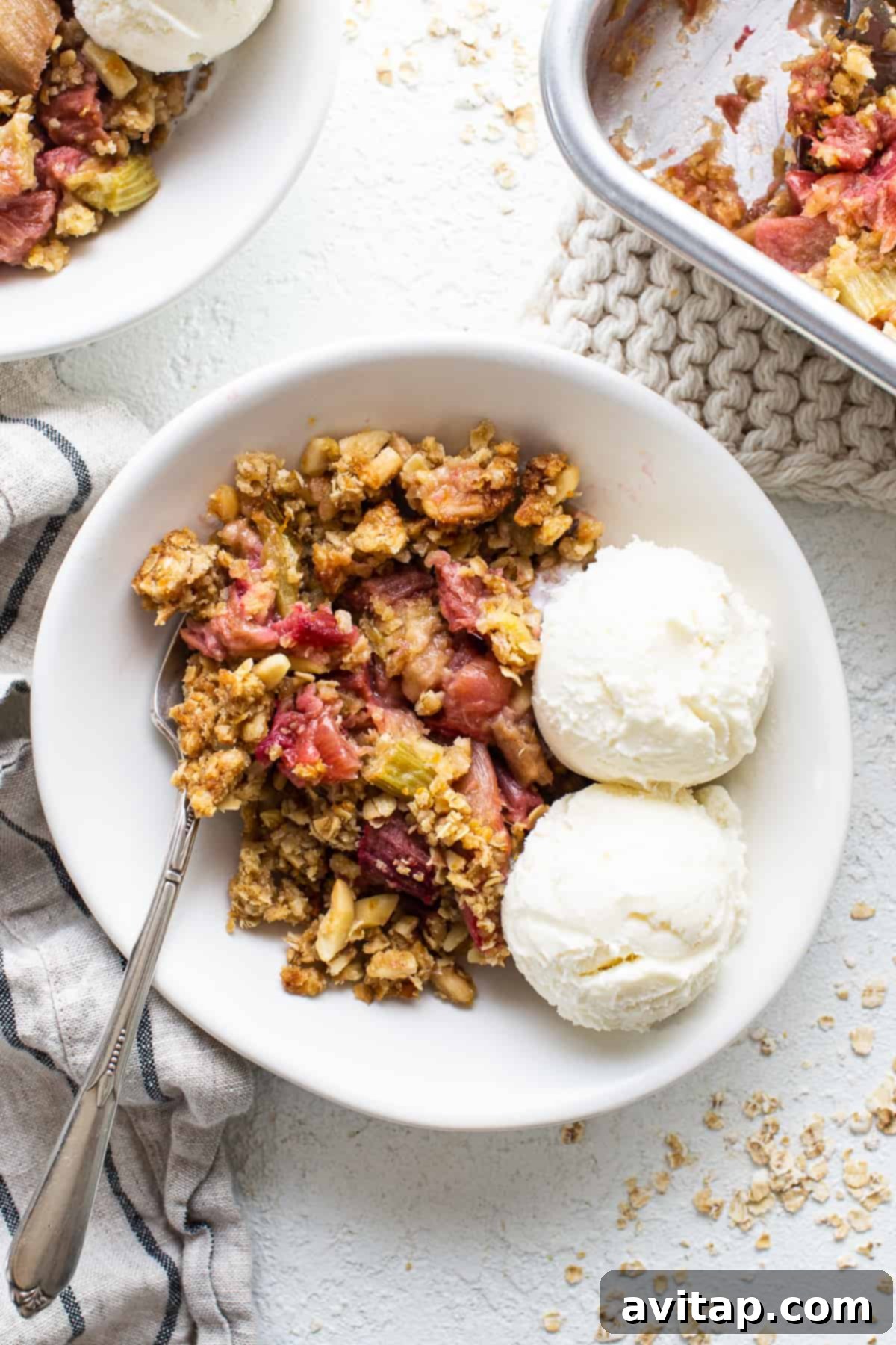A bowl of freshly baked rhubarb crisp topped with a scoop of vanilla ice cream and fresh berries, ready to be enjoyed.