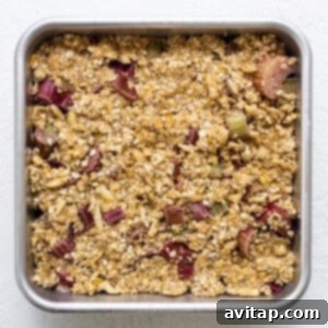 A metal baking pan filled with the rhubarb filling, topped with a generous layer of oat crumble.