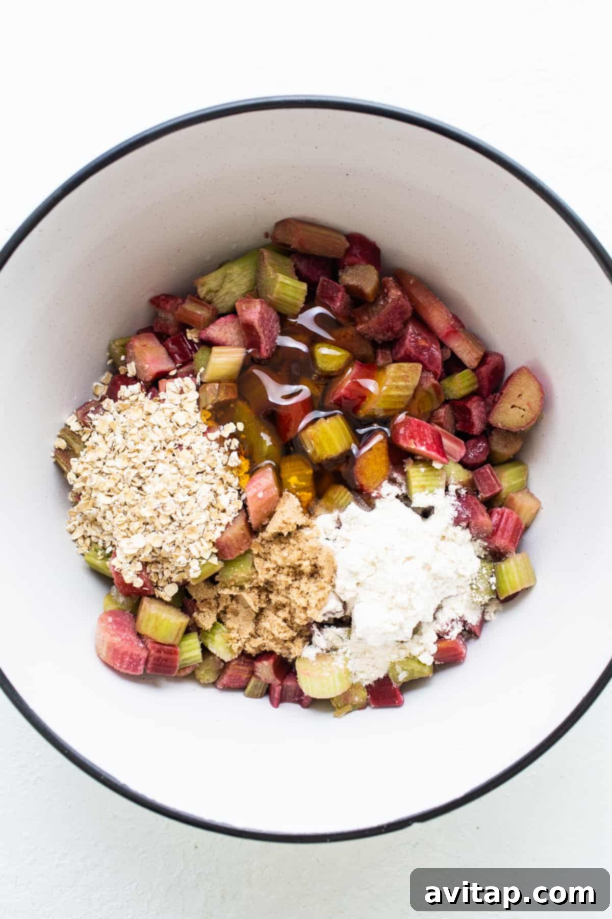 Close-up of chopped rhubarb and oats in a mixing bowl on a white surface, ready for the crisp filling.