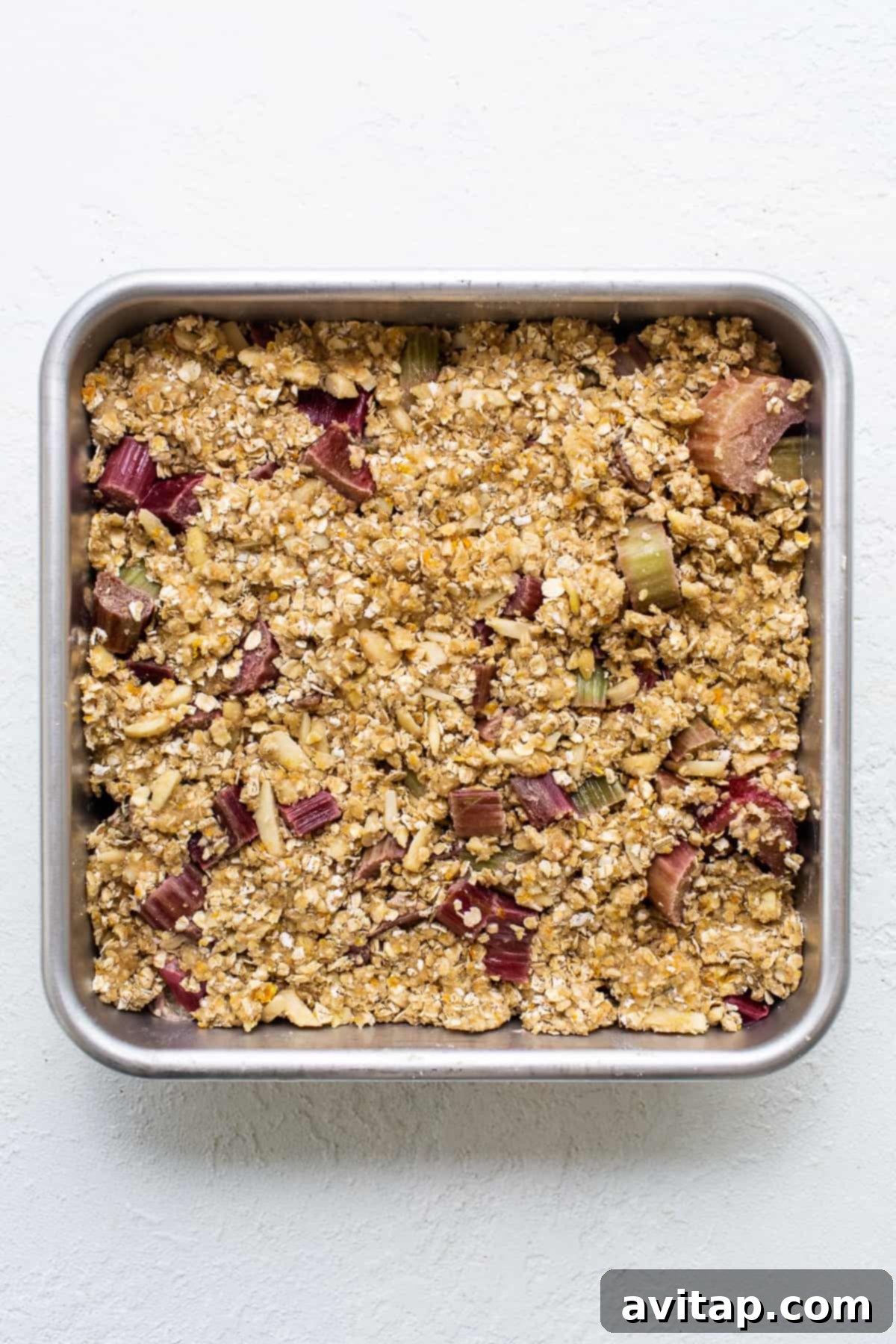 A baking pan filled with the oat crumble topping, ready to be spread over the rhubarb filling.