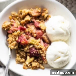 A bowl of rhubarb crisp with ice cream and granola, showcasing the golden topping.