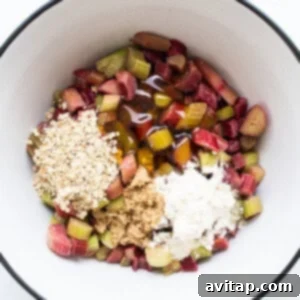 Close-up of chopped rhubarb and oats in a mixing bowl on a white surface, ready for the crisp filling.