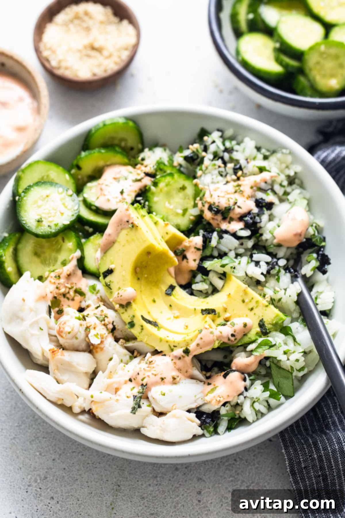 A white bowl with a generous serving of seasoned sticky rice, vibrant green cucumbers, and other fresh ingredients, ready to be topped.