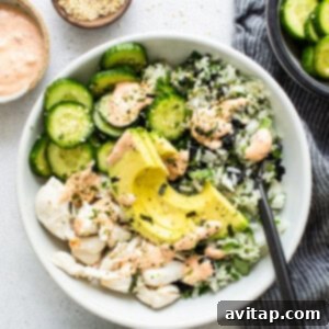 A fully assembled sushi bowl with seasoned rice, cucumbers, crab, avocado, and spicy mayo, ready to be enjoyed.